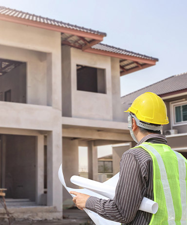 Ingeniero en casco protector y papel de planos en el sitio de construcción de la casa